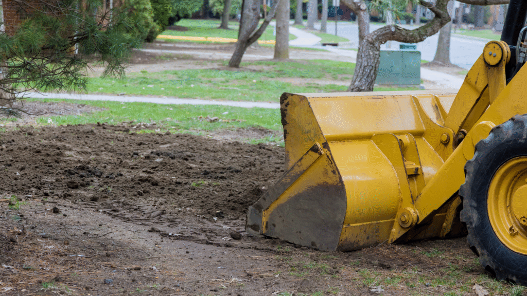 Yellow front-end loader leveling soil during a residential yard grading project by Georgia Roots Landscaping in Warner Robins, GA.