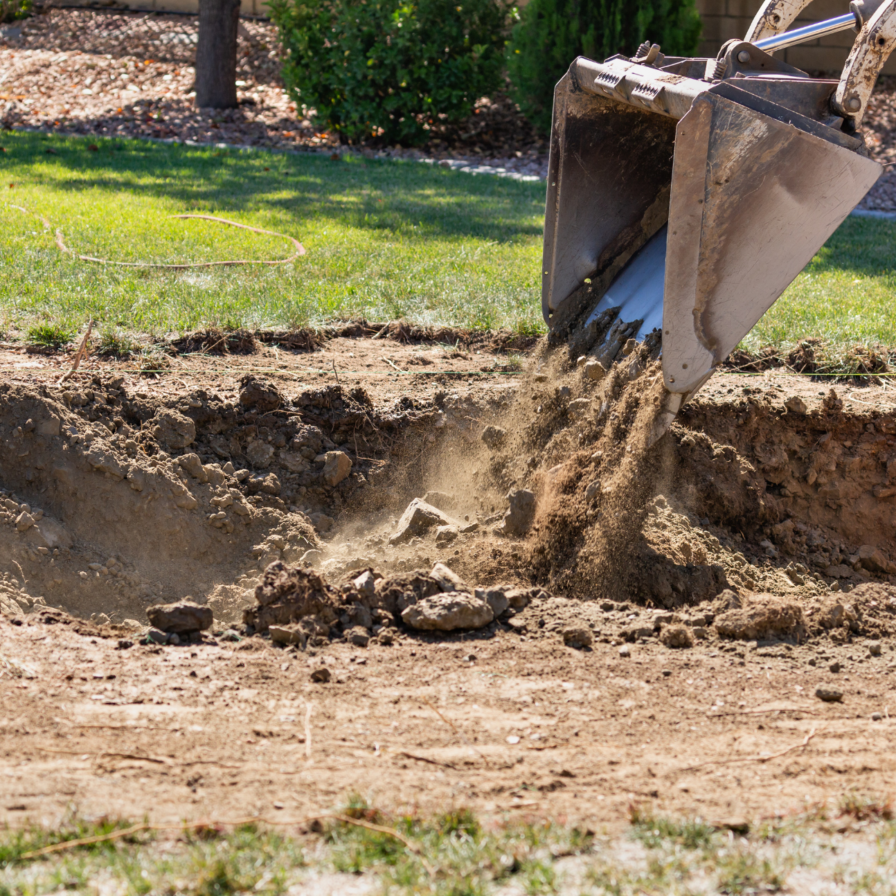 Excavator pouring soil into a backyard excavation site for landscape installation and drainage improvement by Georgia Roots Landscaping in Middle Georgia.
